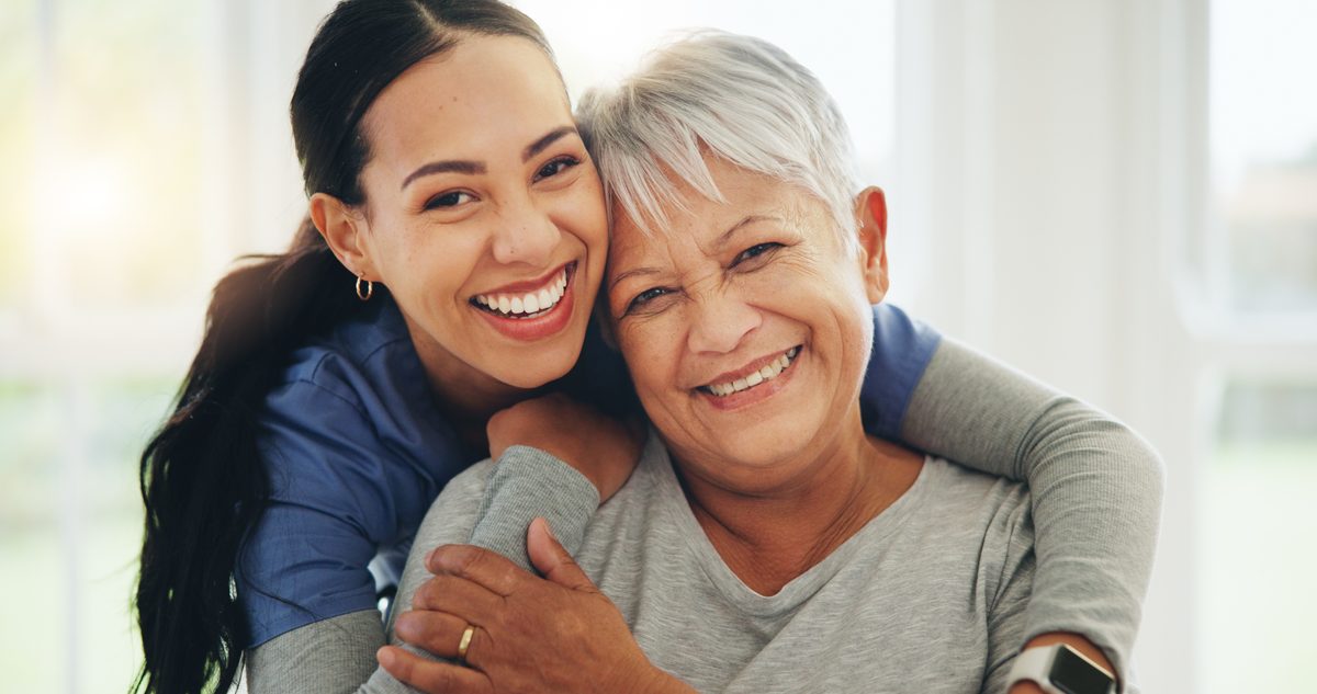 A nurse embracing and comforting a smiling elderly patient during a care visit